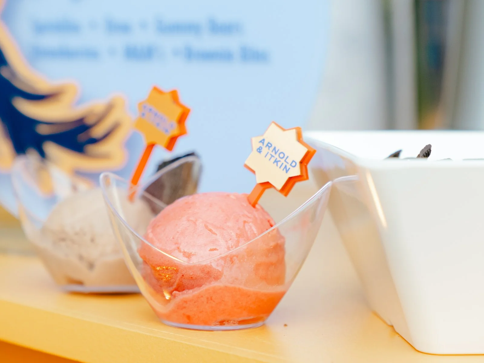 Pink sorbet and cookies and cream ice cream in clear cups with orange star-shaped toppers at an ice cream bar